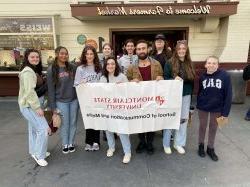 Semester in LA students pose for a photo in front of the Los Angeles Farmers Market, holding a banner that says "Montclair State 大学 School of Communication and Media."