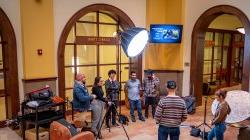 students stand behind camera and lamp, filming other students