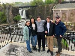 A professor and four students stand in front of a waterfall.