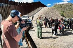 A student with headphones and a camera films a scene at the border of Mexico and Arizona.